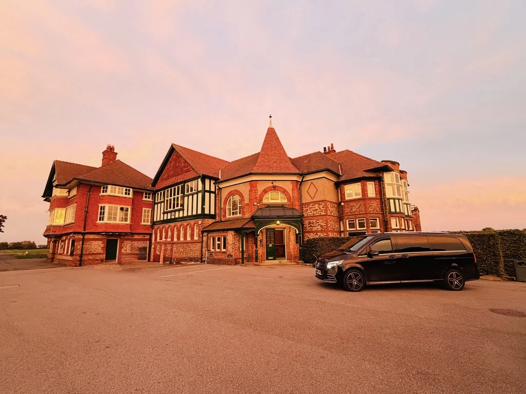 Golf tours UK: a black Mercedes-Benz V-Class golf chauffeur car outside the clubhouse at Royal Lytham and St Annes at sunset