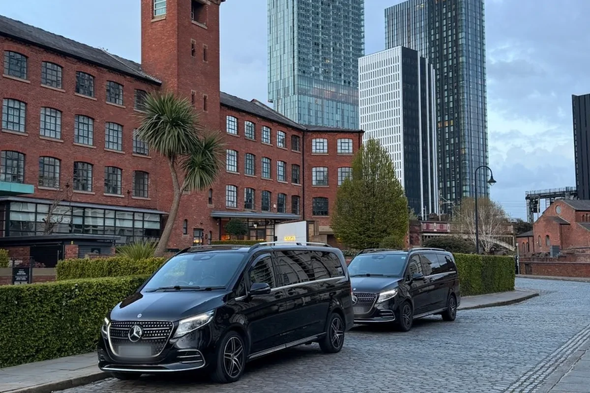 Two black Mercedes-Benz V-Class chauffeur cars on the cobbles in Castlefield with the Manchester skyline behind