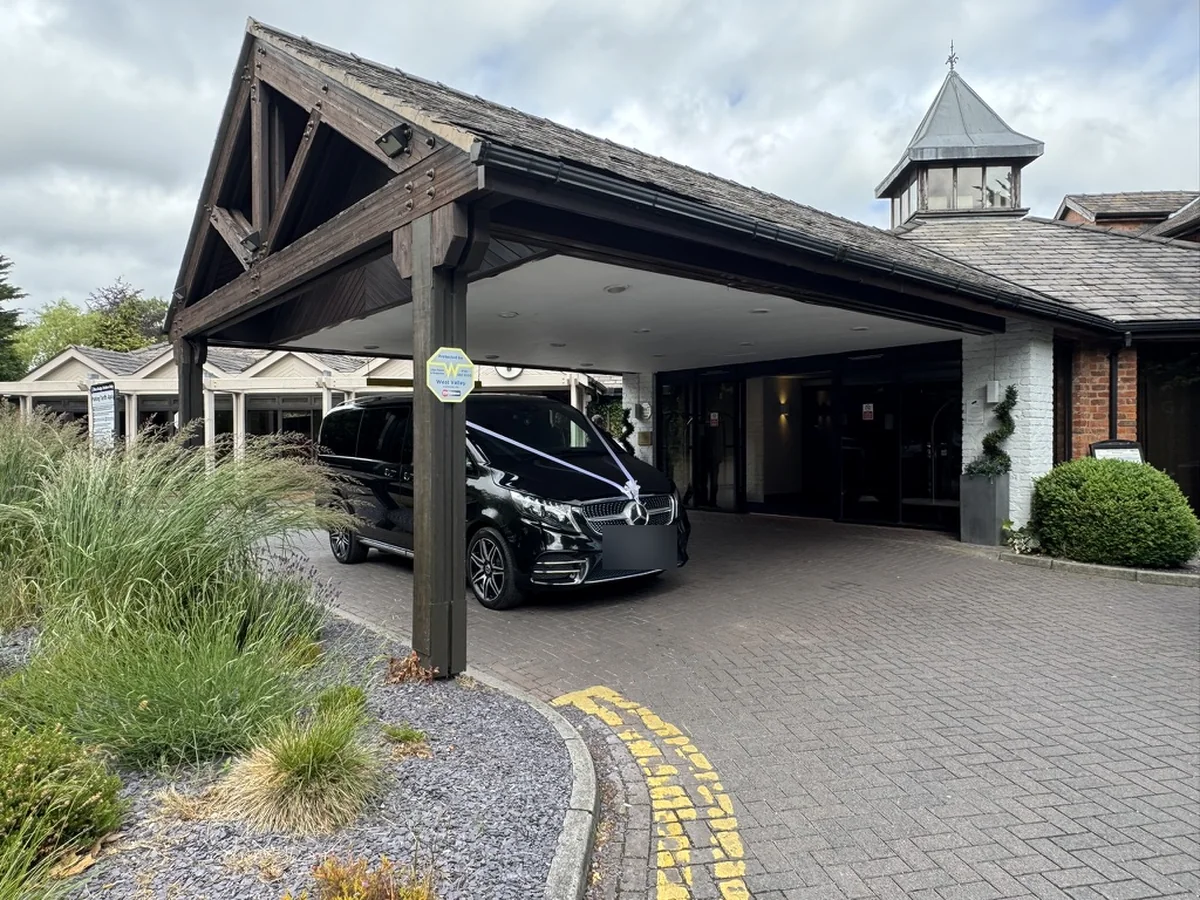 Wedding car hire Manchester: black Mercedes-Benz V-Class dressed with white ribbons at a hotel entrance